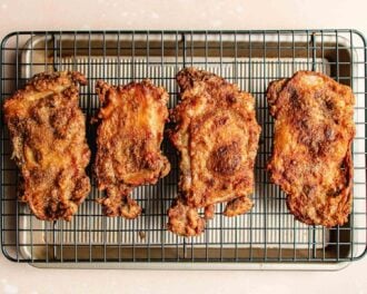 Four pieces of crispy, golden-brown honey garlic chicken thighs cooling on a wire rack set over a baking sheet.