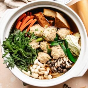 A chicken meatball hot pot filled with assorted vegetables, tofu, mushrooms, and leafy greens, all arranged neatly in a flavorful broth.