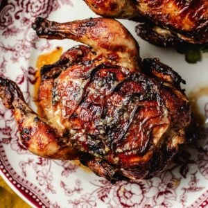 A golden-brown roasted Cornish hen with crispy skin, made using the air fryer cornish hens method, sits on a decorative red and white plate.