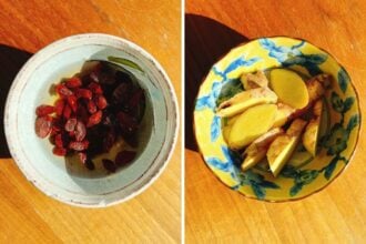 Two ceramic bowls on a wooden surface; the left holds dried red goji berries soaked in rice wine, perfect for adding to sesame oil chicken soup, while the right displays sliced fresh ginger root in a yellow floral-patterned dish.
