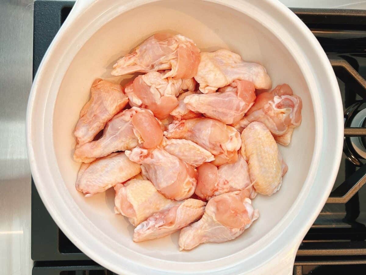 A white bowl filled with raw chicken wings sits on a stovetop, ready to be transformed into a flavorful sesame oil chicken soup.