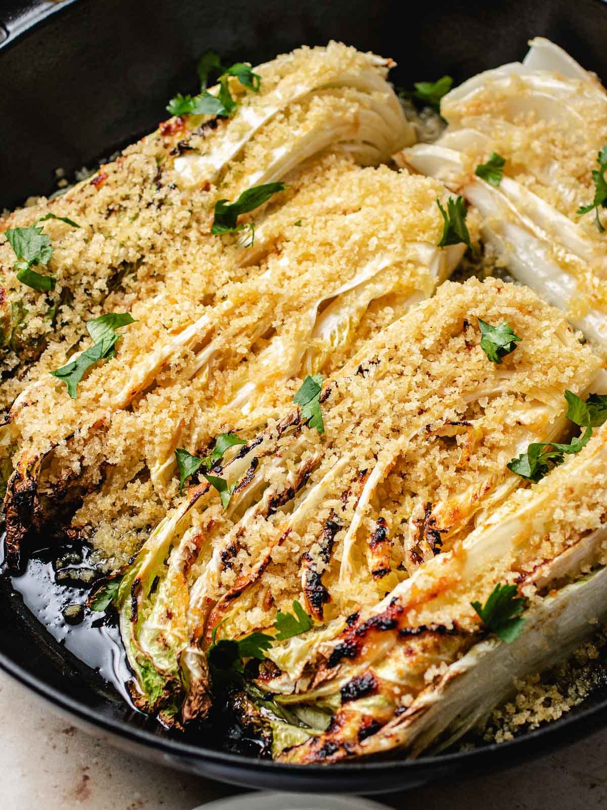 Roasted napa cabbage wedges topped with golden panko breadcrumbs and chopped fresh herbs, arranged in a black cast iron skillet.