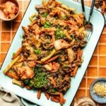 A platter of Bulgogi Fries featuring crinkle-cut fries topped with kimchi, green onions, sesame seeds, shredded cheese, and seasoned beef on a light blue tray, served with a fork and knife on the side.