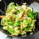 A black wok filled with Taiwanese Cabbage and slices of crispy garlic cjo[s, stir-fried to a light, glossy sheen—a dish reminiscent of Din Tai Fung’s signature style.