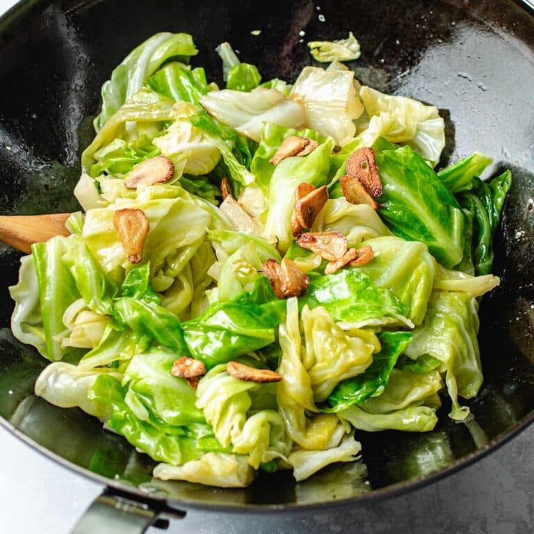 A black wok filled with Taiwanese Cabbage and slices of crispy garlic cjo[s, stir-fried to a light, glossy sheen—a dish reminiscent of Din Tai Fung’s signature style.