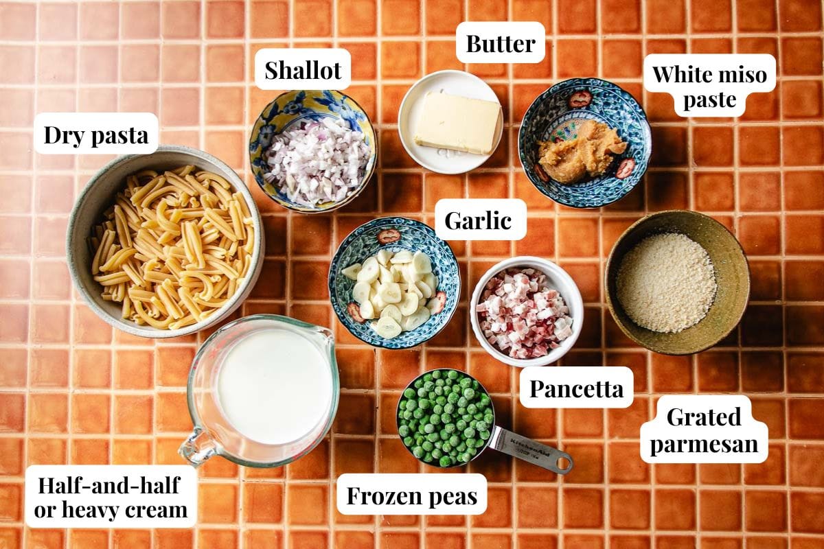 A variety of ingredients in bowls on a tile surface with individual ingredients to make miso pasta.