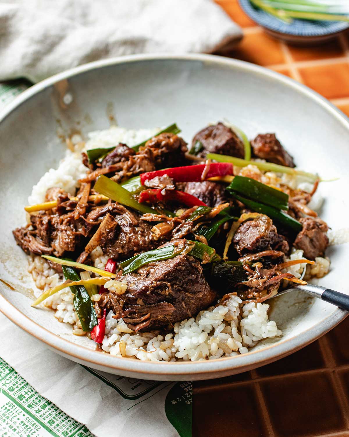 A bowl of steamed white rice topped with tender braised pork, sliced green onions, and red and green chili peppers, served with a fork—perfect for fans of Mongolian Pork Slow Cooker flavors.