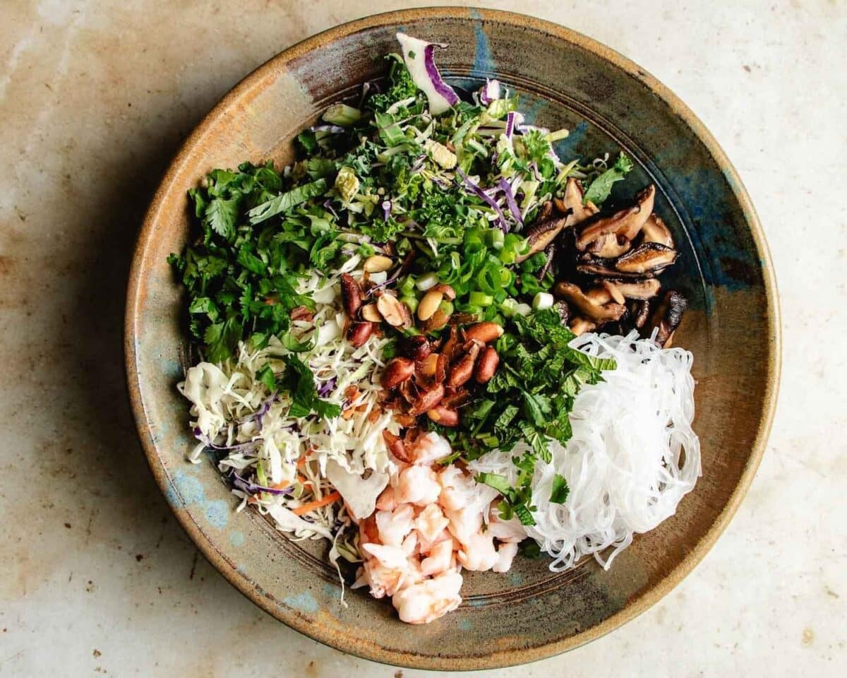 A spring roll in a bowl featuring glass noodles, shrimp, cooked mushrooms, chopped herbs, peanuts, shredded cabbage, and greens—all artfully arranged in separate sections on a rustic plate - representing a real spring roll filling in Asian cuisine.