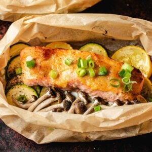 Miso butter salmon fillet baked in parchment paper, topped with chopped green onions, served over mushrooms and sliced zucchini and yellow squash.