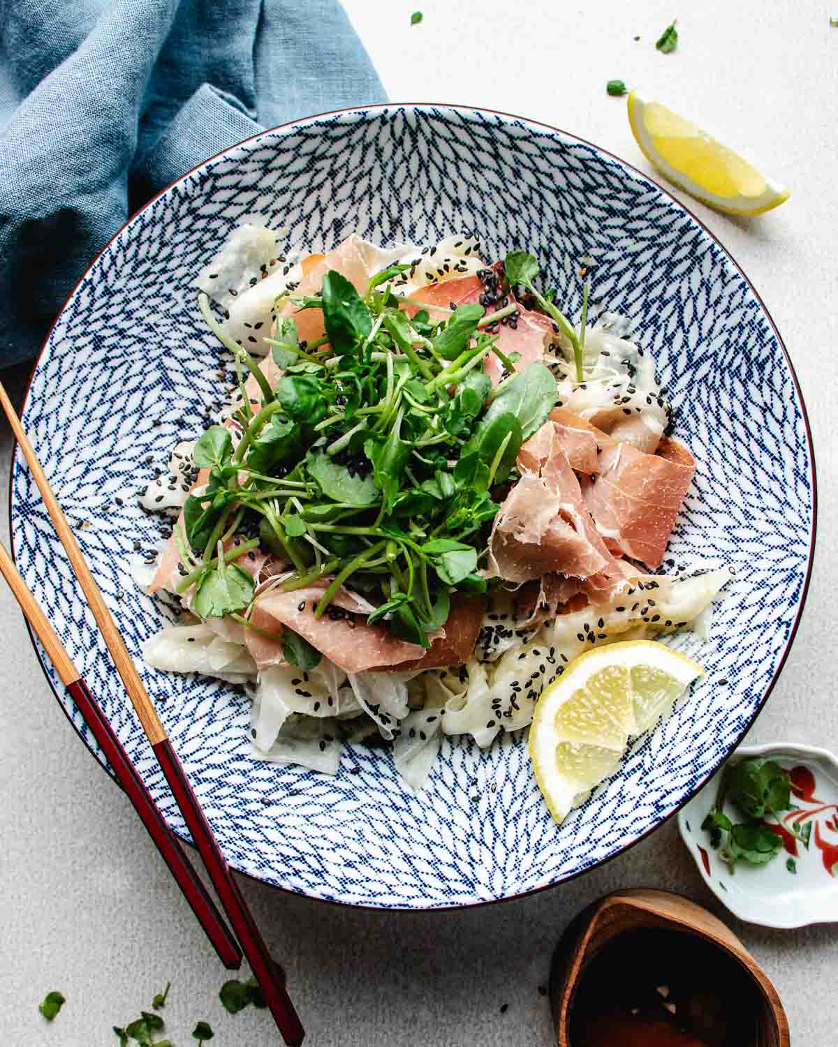 a large blue and white salad bowl filled with shaved daikon ribbons, prosciutto, watercress, and lemon dressing. A cool and refreshing daikon salad perfect for summer days.