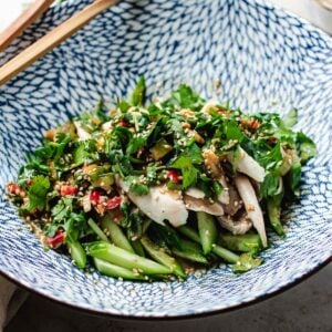 A patterned blue and white bowl filled with Bang Bang Chicken Taiwanese Style—sliced chicken, cucumber, herbs, red chili, and sesame seeds—served with wooden chopsticks resting on the rim.