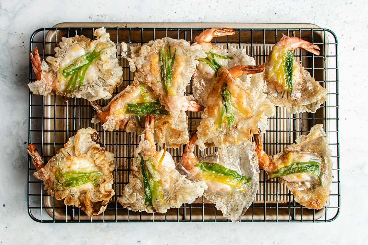 Crispy fried shrimp wrapped in thin rice paper sheets are topped with green onions and served alongside rice paper shrimp chips, all arranged on a wire cooling rack set over a baking sheet.