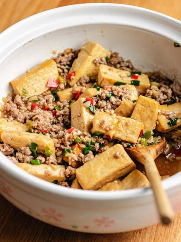 A ceramic bowl filled with tofu cubes, minced pork, chopped green onions, and red chili, with a wooden spoon for serving—perfect for enjoying classic tofu with minced pork.