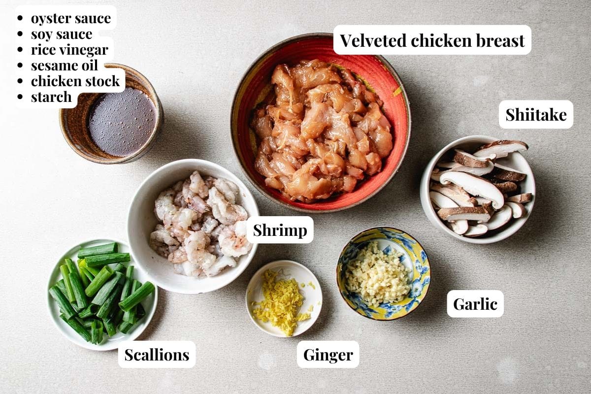 Bowls contain sliced and marinated chicken breast, shrimp, shiitake mushrooms, chopped garlic, ginger, scallions, and sauce ingredients labeled: oyster sauce, soy sauce, rice vinegar, sesame oil, chicken stock, and starch—everything you need for a flavorful Chicken and Shrimp Stir Fry.
