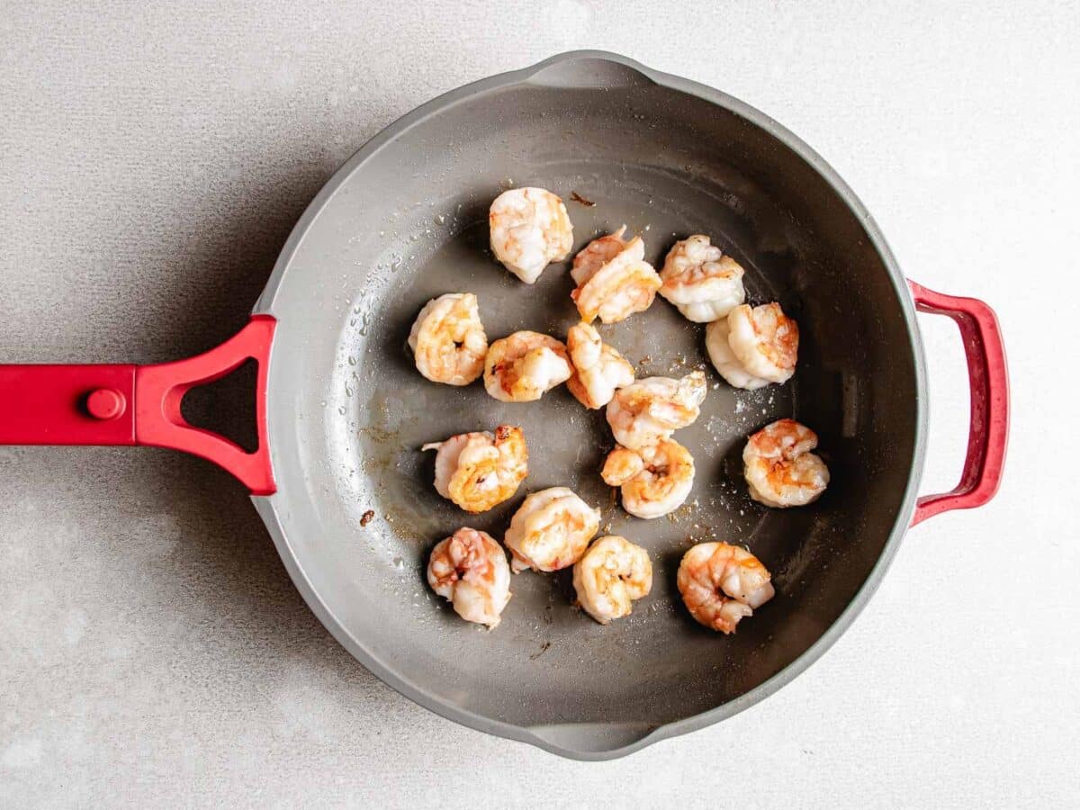 Seared shrimp pieces in a gray nonstick skillet with a red handle, arranged in a single layer on a light-colored countertop, ready to be added to your favorite Chicken and Shrimp Stir Fry.