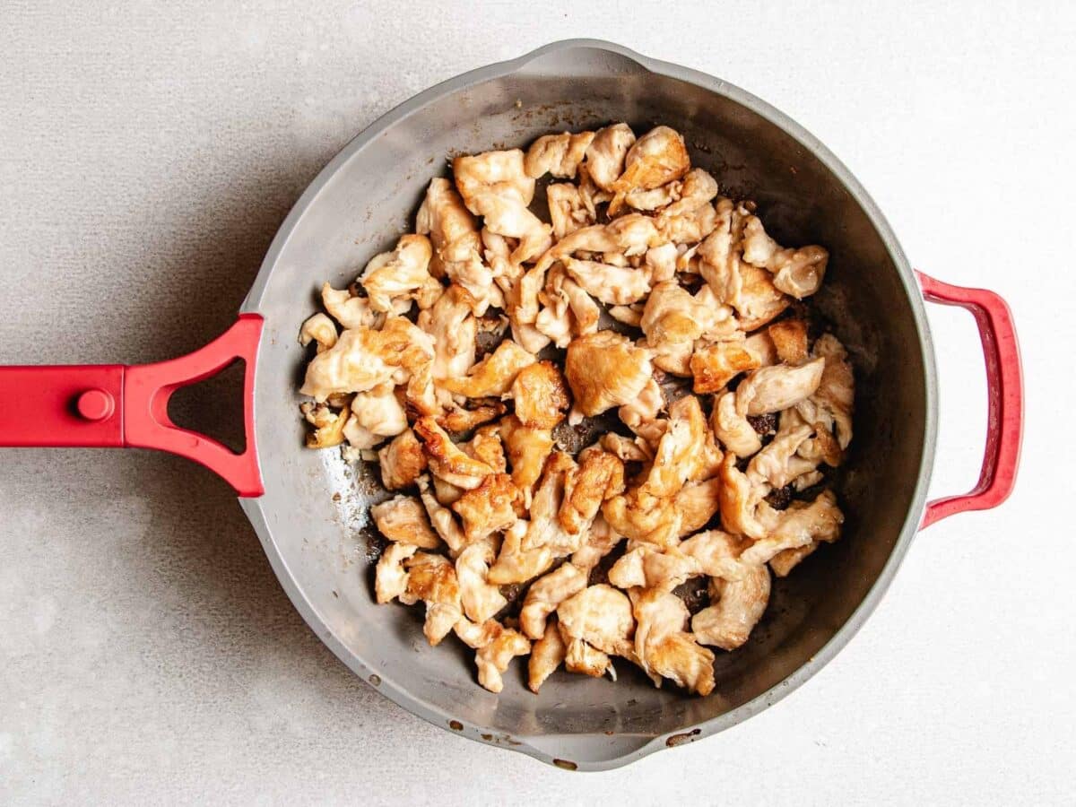 Stir fried pieces of chicken breast in a gray skillet with a red handle, sitting on a light countertop, make the perfect base for a delicious Chicken and Shrimp Stir Fry.