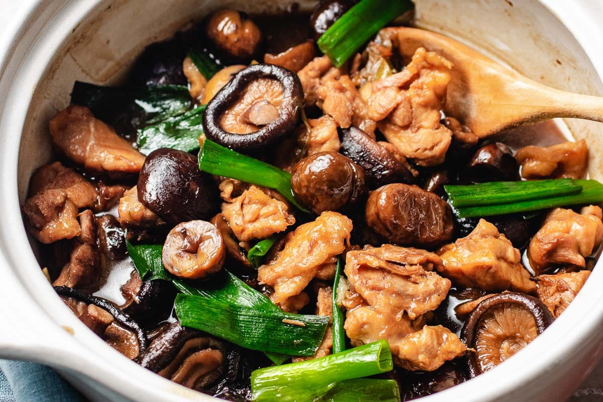 Chinese braised chicken with shiitake mushrooms, chestnuts, and green onions served in a white ceramic pot.