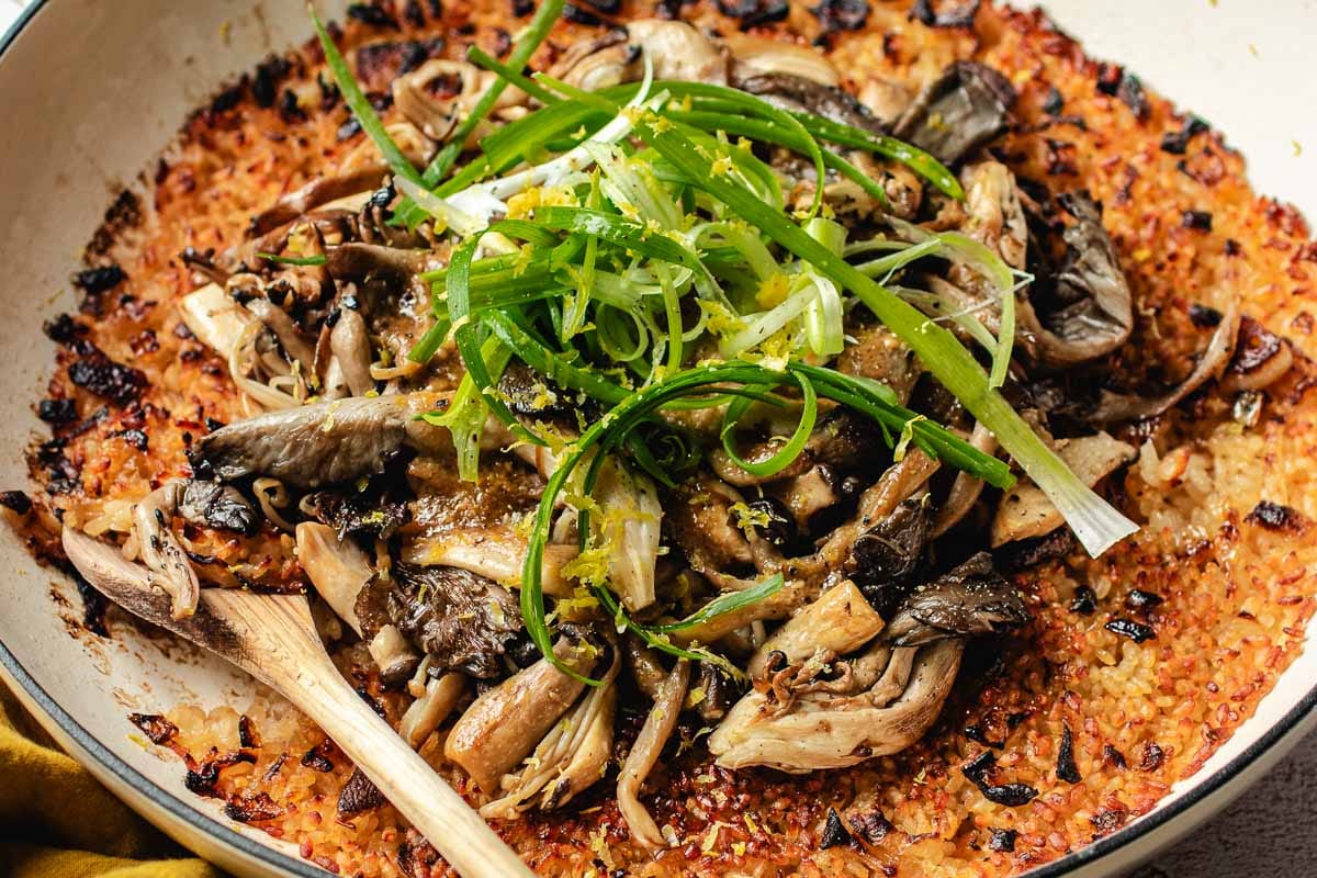 A pan of miso mushroom crispy rice topped with sliced green onions, with a wooden spoon resting in the bowl.