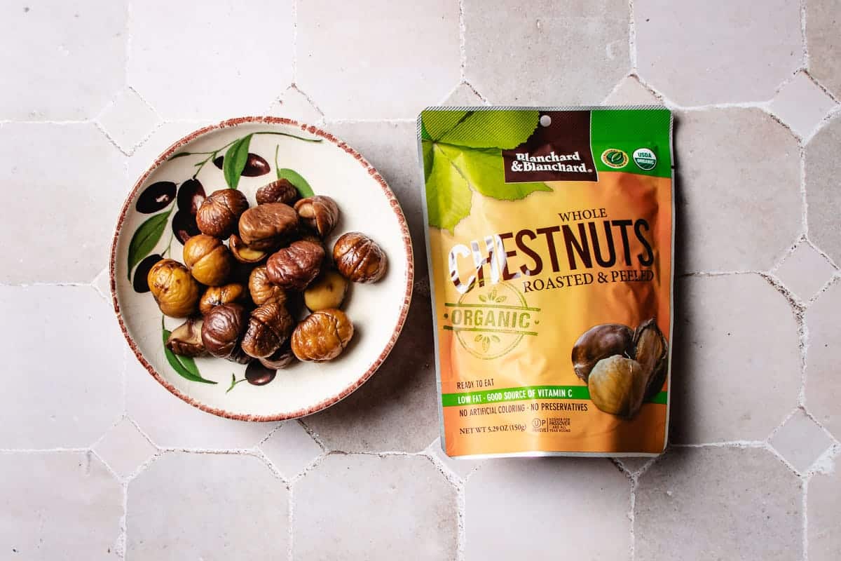A bowl of roasted peeled chestnuts, perfect for Chinese braised chicken with chestnuts, sitting next to a package of Blanchard & Blanchard organic whole roasted chestnuts.