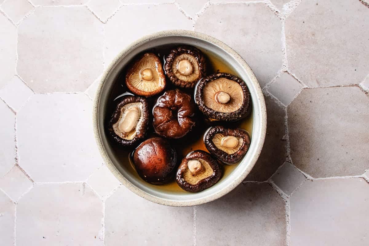 A ceramic bowl filled with shiitake mushrooms soaking in a broth for Chinese braised chicken with chestnuts.
